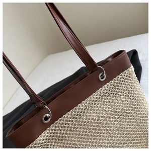 Detail of woven straw tote bag featuring dark brown leather trim and silver metal eyelets