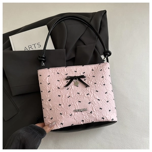 Close-up of pink bucket bag with black bow detail and metal fashion logo lettering