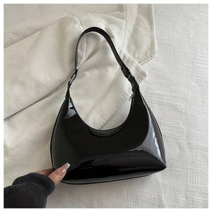 Detail of black patent leather underarm bag with glossy finish and silver buckle