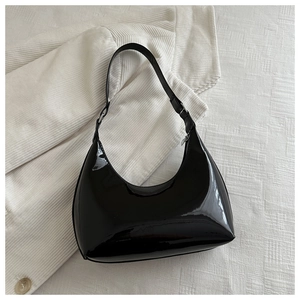 Detail of glossy black patent leather shoulder bag with silver buckle on textured fabric