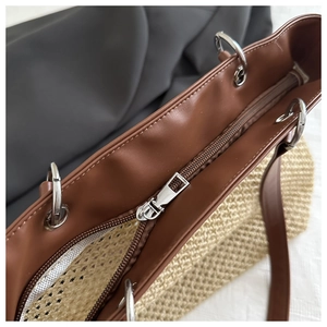Detail of straw tote bag with brown leather trim and silver metal zipper closure