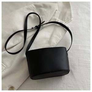 Flat lay of a black matte bucket bag with adjustable strap on white textured background