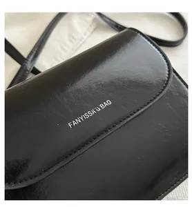 Detailed close-up of a black glossy leather crossbody bag with silver FANYISSA text logo