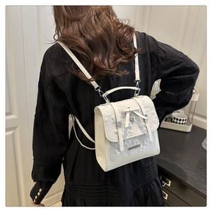 Detail of white lace bow backpack with heart pendant and metallic fashion logo