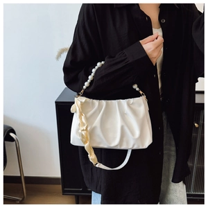Detail of white pleated cloud bag with pearl handle and pale yellow ribbon decoration