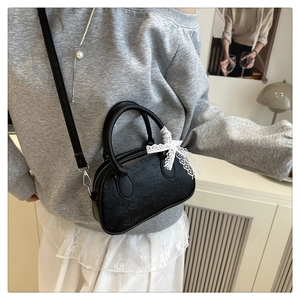 Dettaglio della mini borsa nera goffrata con fiocco in pizzo bianco decorativo sul manico