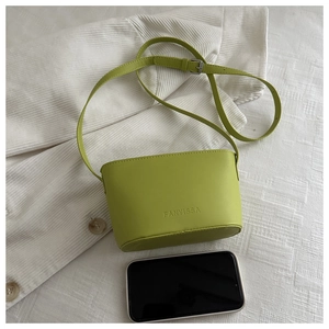 Avocado green leather bucket bag with embossed logo and adjustable strap next to a phone