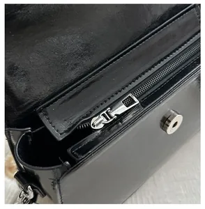 Macro view of smooth silver zipper and magnetic clasp on black glossy leather saddle bag
