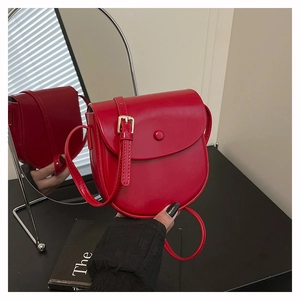 Detail of red leather saddle bag with gold metal buckle and adjustable shoulder strap