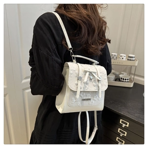 Detail of white leather backpack with delicate lace embroidery and metal heart pendant