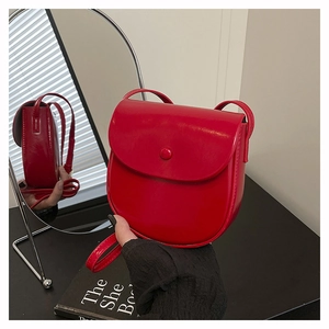 Detail view of red glossy leather saddle bag showing the round clasp and side structure