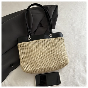 Close-up of woven straw tote bag with black leather straps and metal grommet details