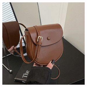 Detail of caramel brown saddle bag with matte leather finish and golden buckle hardware