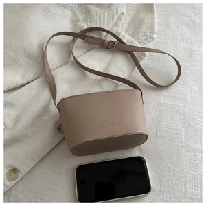 Flat lay of a beige bucket bag on white fabric with a phone showing its compact size
