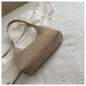 Close-up of glossy patent leather half-moon shoulder bag in elegant apricot on fabric