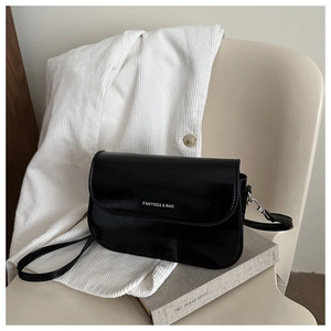 Detail view of the glossy black leather flap bag with white branding and silver hook