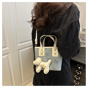 Detalle de bolso tipo cubo azul claro con estampado de mariposa y dije de perro