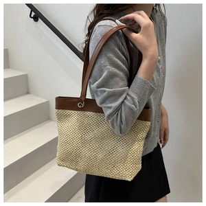 Detail of woven tote bag showing brown leather shoulder straps and metal buckle connection
