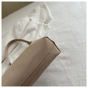 Detailed view of fine stitching and glossy patent leather on a beige shoulder bag