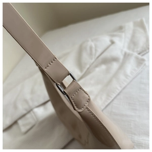 Detailed shot of silver D-ring buckle and neat stitching on beige patent leather bag