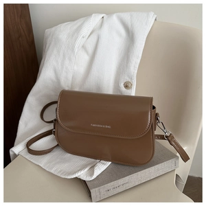 Close-up of brown leather crossbody bag with letter print resting on a book