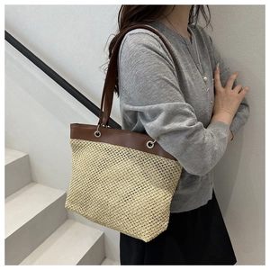 Detail of woven straw texture and dark brown leather straps on large summer tote bag