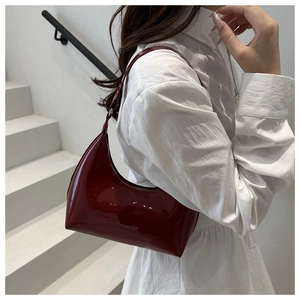 Detail of burgundy patent leather crescent bag on a model in a minimalist urban setting