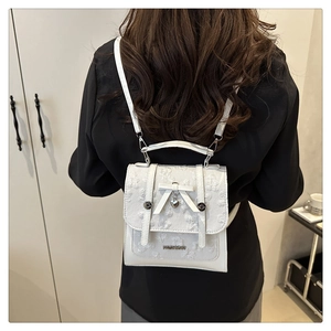 Close-up of white jacquard mini backpack featuring butterfly lock and heart pendant detail