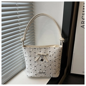 Detail of white textured shoulder bag featuring black butterfly patterns and ribbon bow