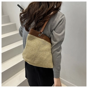 Close-up of woven straw tote bag featuring brown leather trim and metallic buckles