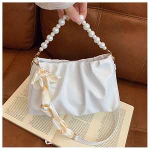White ruched cloud bag with pearl handle and yellow silk scarf detail on a leather sofa