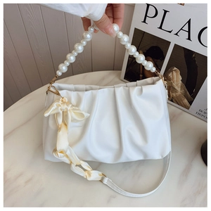 Close-up of white pleated cloud bag featuring pearl handle and silk bow detail