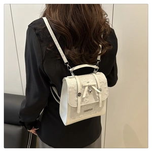 Detail of white backpack with floral lace texture, silver heart pendant, and bow accent
