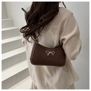 Back view of a model wearing a brown leather shoulder bag with a gold bow detail