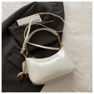 Close-up of white patent leather shoulder bag with gold chain and cherry charm detail