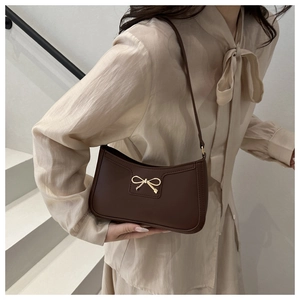 Close-up of a dark brown underarm bag with a golden metal bow accessory on a white background