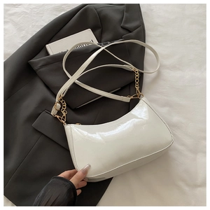 Close-up of white patent leather crescent bag with gold chain on grey blazer