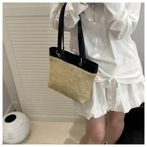 Detail of hand-woven straw tote bag with black leather handles and silver metal studs