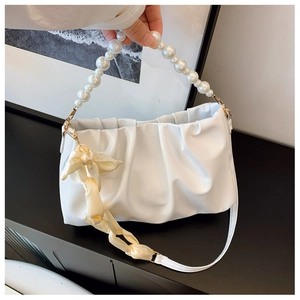 Close-up of white pleated cloud bag featuring a large pearl handle and silk ribbon