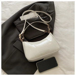 Detail of white patent leather hobo bag with gold chain strap on a blazer background