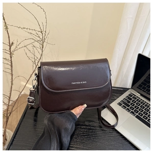 Detail of dark brown glossy leather shoulder bag with white printed logo on the flap