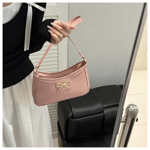 Pink underarm bag with gold bow detail shown in a hand-held lifestyle setting