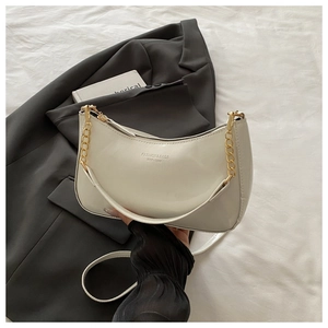 Detail of white patent leather hobo bag with gold chain on dark grey suit jacket