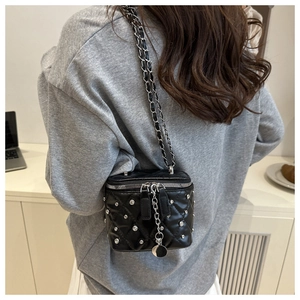 Detail of a quilted crossbody box bag with studs and chain strap on a grey hoodie
