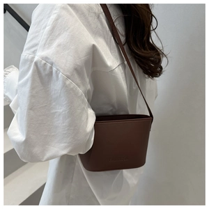Deep brown bucket bag shown on shoulder with embossed logo detail and sleek leather texture