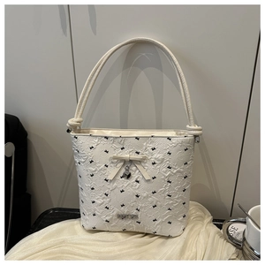 Close-up of off-white textured bucket bag with black bow patterns and silver heart charm