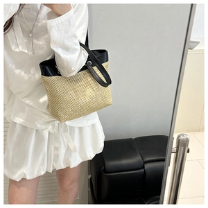 Detailed view of the woven straw tote bag with black leather straps and metal rings