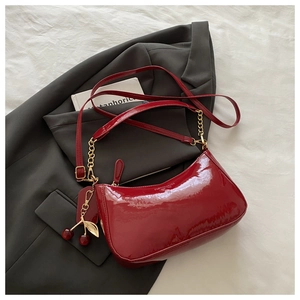 Close-up of burgundy patent leather bag with cherry charm and gold chain detail