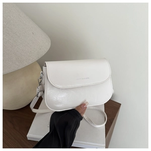 Detail of white matte PU leather saddle bag with silver logo on a wooden table