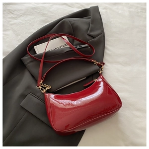 Close-up of a glossy red patent leather underarm bag with gold chain on a grey blazer